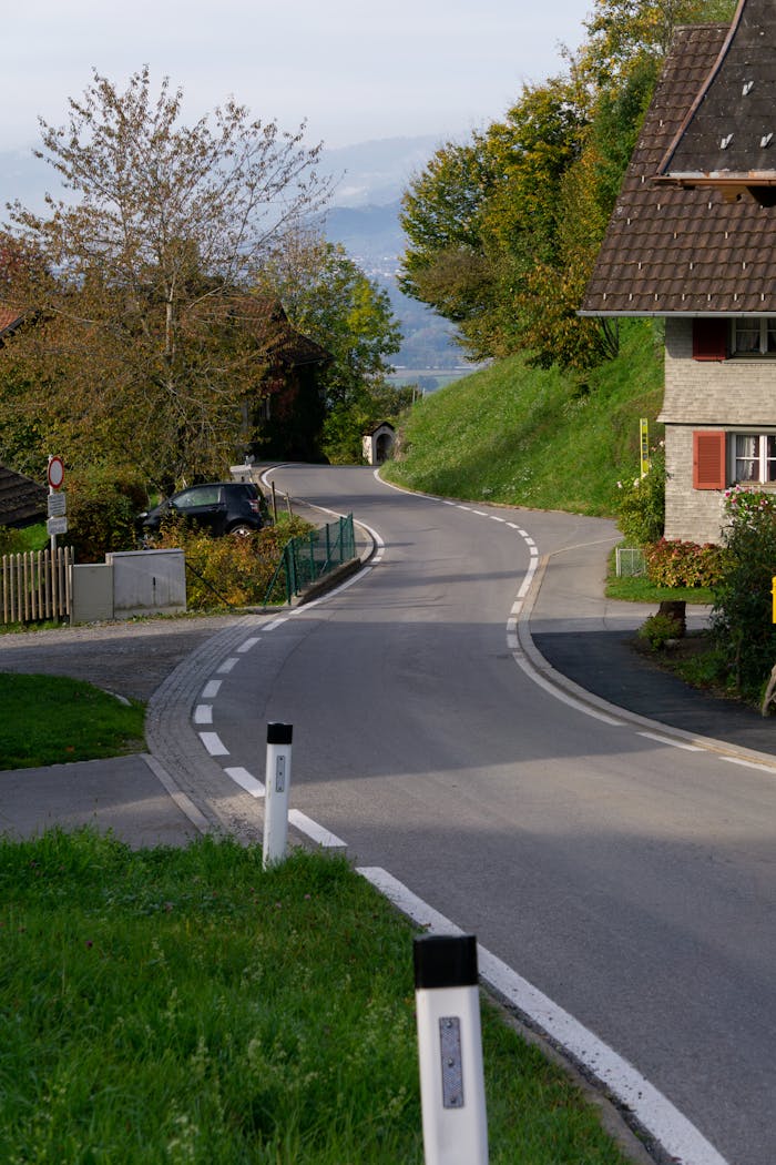 A picturesque winding road through a quaint rural village surrounded by lush greenery and cozy houses.